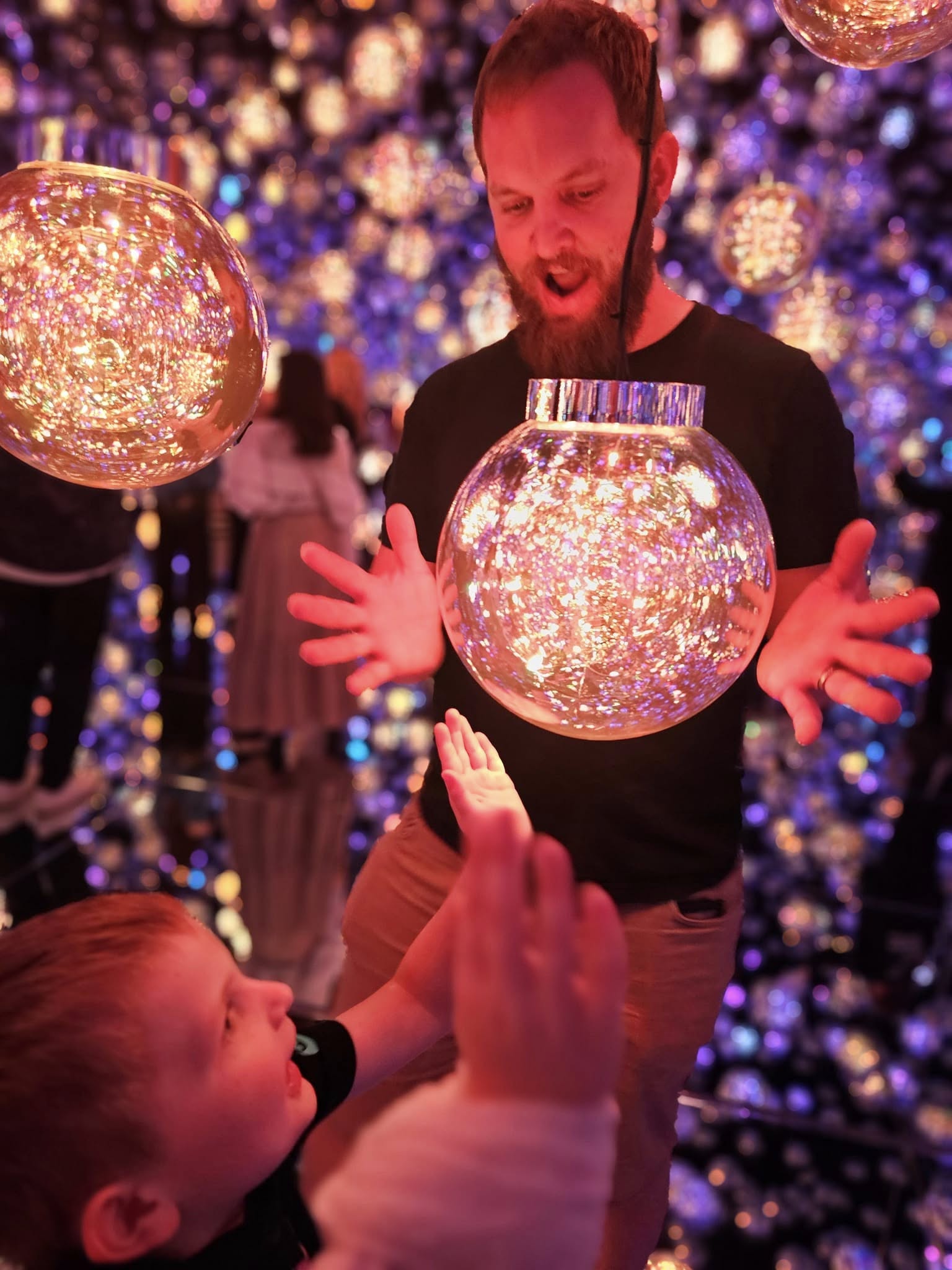 Two people interacting with glowing, reflective orbs against a colorful, blurred background